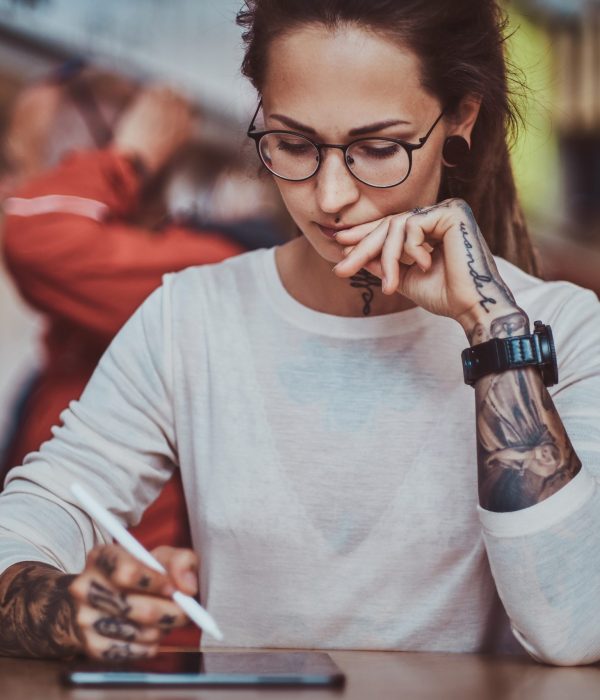Young pretty woman with tattooes on her hands is enjoying her time at food court with her sketching pad.